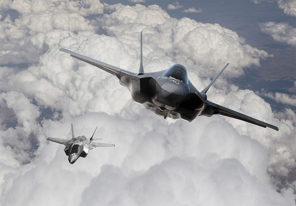 Two advanced fighter jets flying through a cloud-filled sky, showcasing Northrop Grumman's cutting-edge technology in electronic warfare simulation.