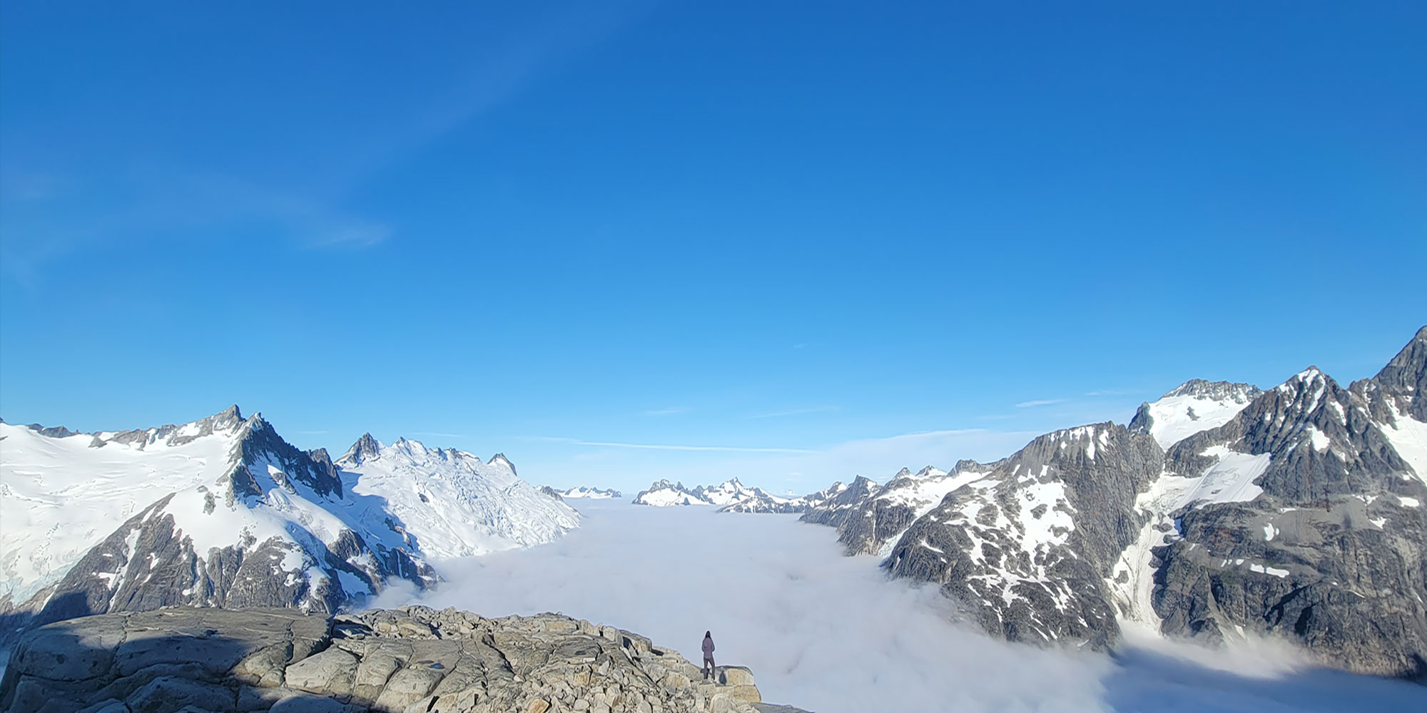 moon-base-hero A person stands on a rocky cliff and stares out snow-capped mountains and clouds.